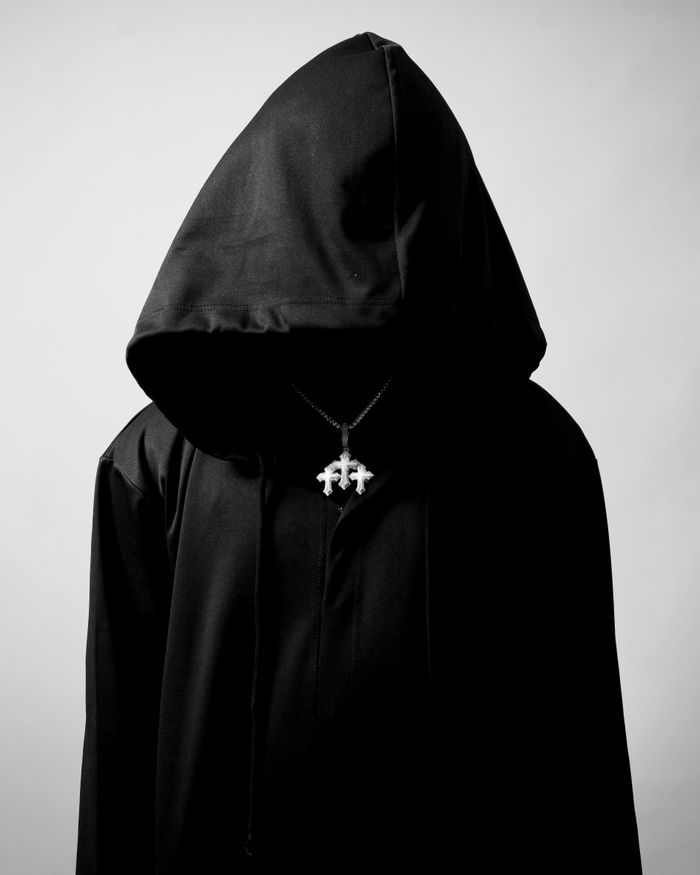 A hooded figure in a black cloak with a mysterious vibe, wearing a pendant.